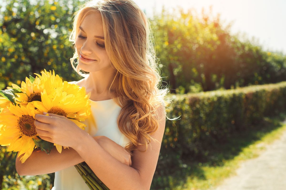 The woman is holding sunflower while sunlight striking her hair.
